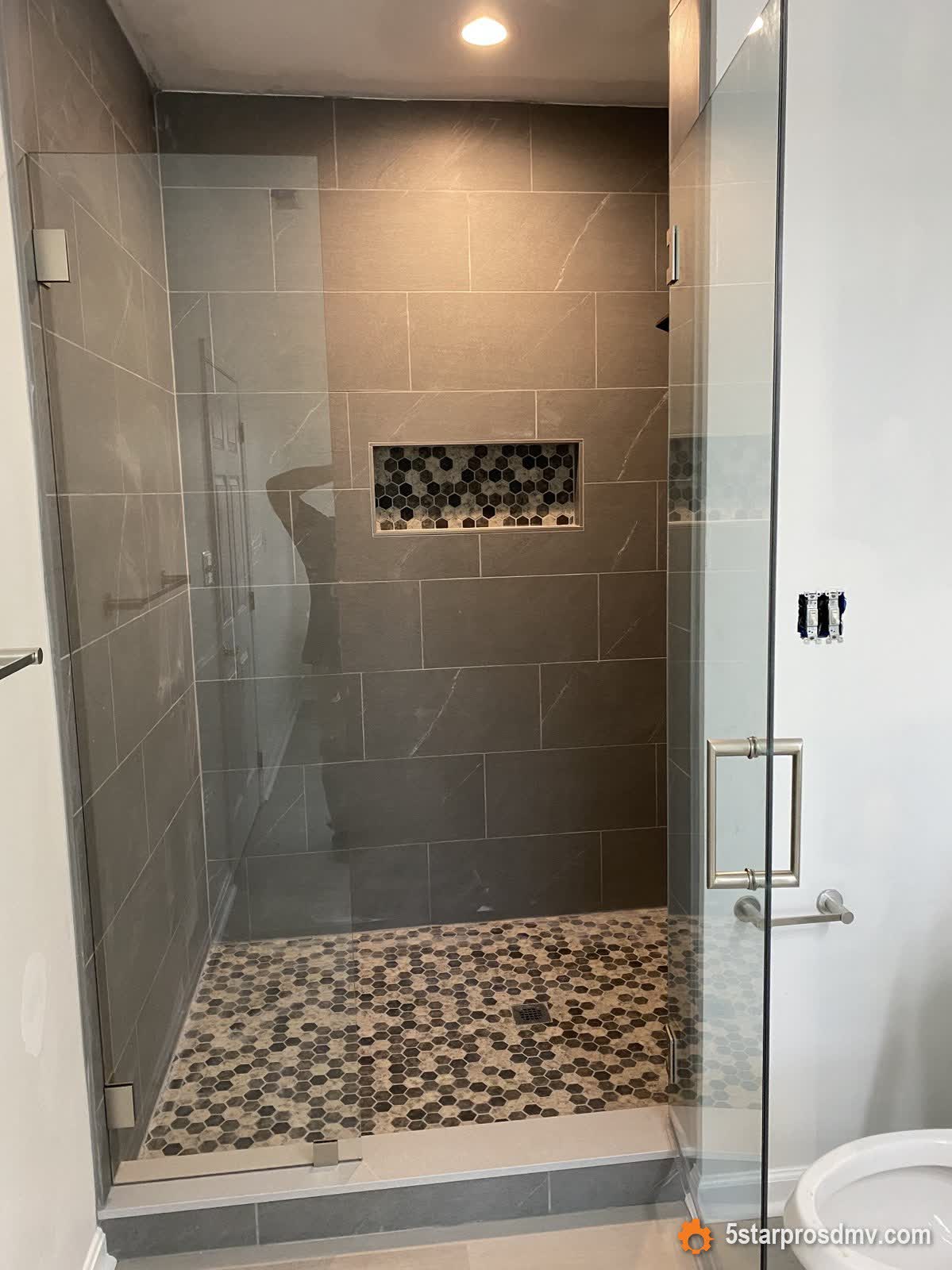 Ducha amplia de vidrio sin marco con azulejo símil mármol gris y piso de mosaico hexagonal por 5 Star Pros DMV