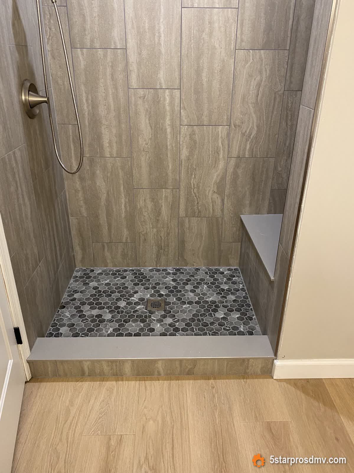 Ducha amplia con azulejo gris símil madera, piso de mosaico hexagonal y banca integrada por 5 Star Pros DMV