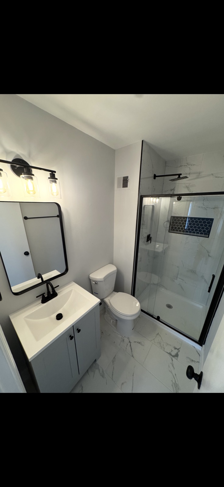Bathroom remodel with marble tile, black fixtures, glass shower enclosure by 5 Star Pros DMV