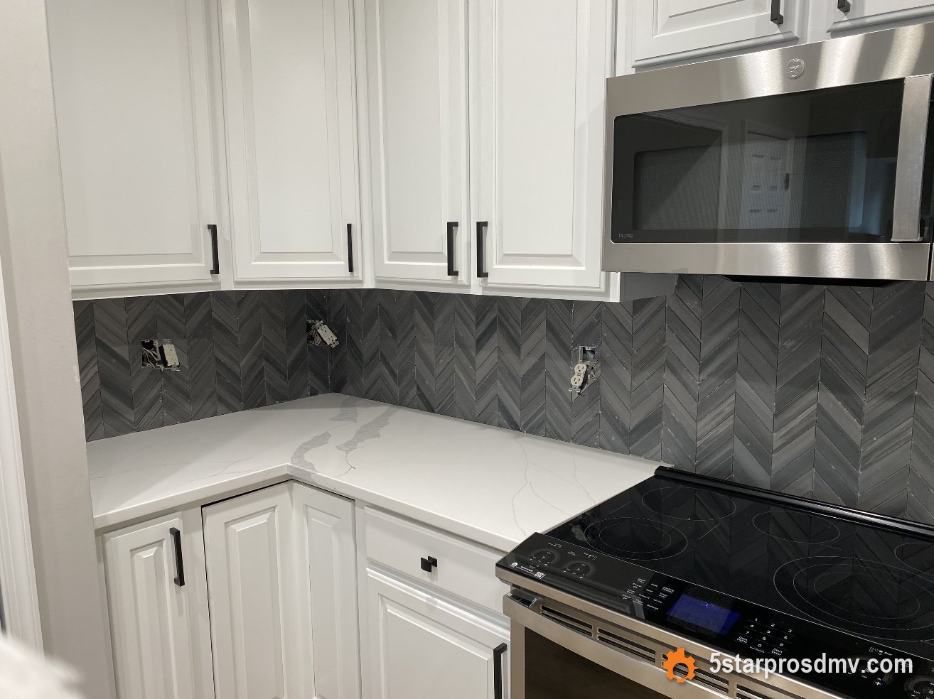 Cocina blanca con salpicadero de azulejo chevron gris, encimera de cuarzo y estufa de acero inoxidable por 5 Star Pros DMV