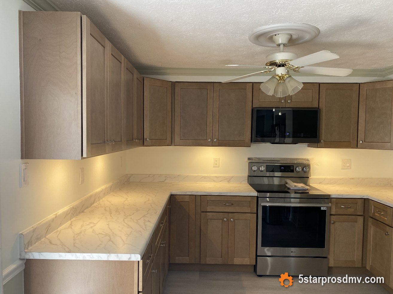 Cocina con gabinetes de madera, encimeras de cuarzo símil mármol e iluminación bajo gabinetes por 5 Star Pros DMV