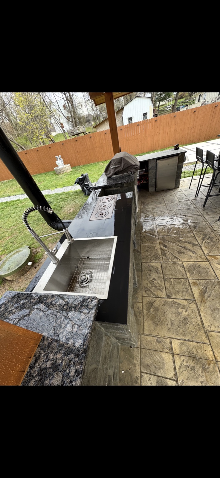 Completed outdoor kitchen with black granite countertop, sink, and burners under covered patio, 5 Star Pros DMV
